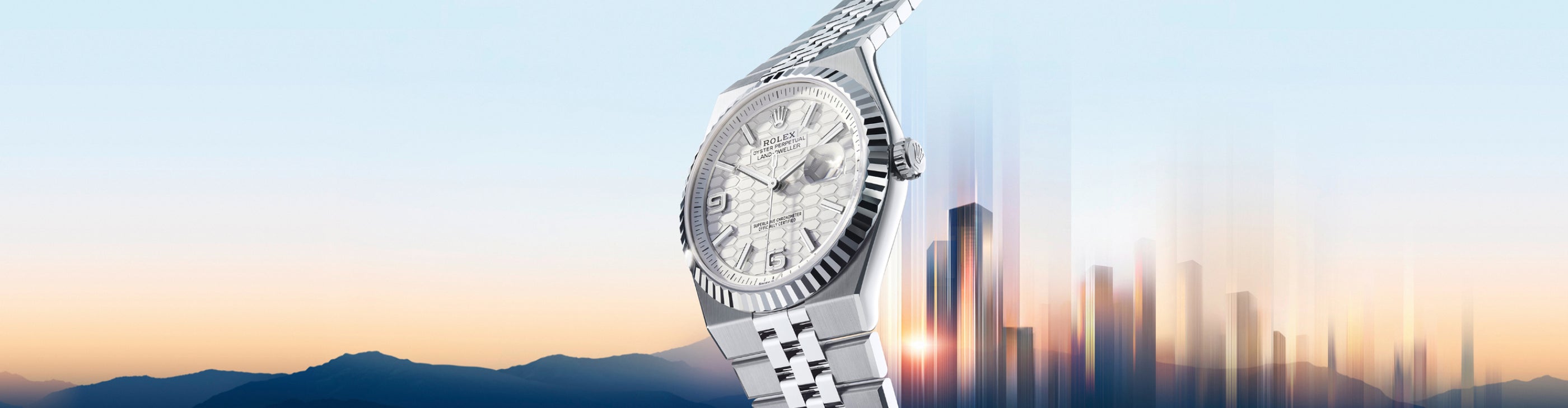 Silver wristwatch with textured dial, set against a blurred cityscape and mountain background at sunrise.