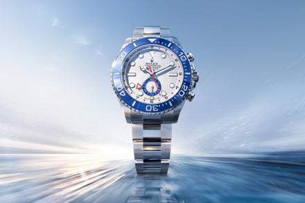 Luxury watch with blue and red accents on a reflective surface with a blue sky background