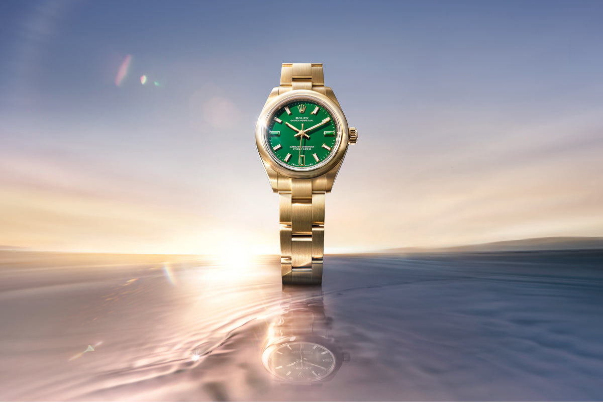 Gold watch with a green face on a reflective surface with a sunset background