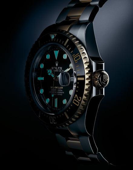A close-up of a luxury Rolex dive watch with glowing blue hour markers and a black and gold bezel.