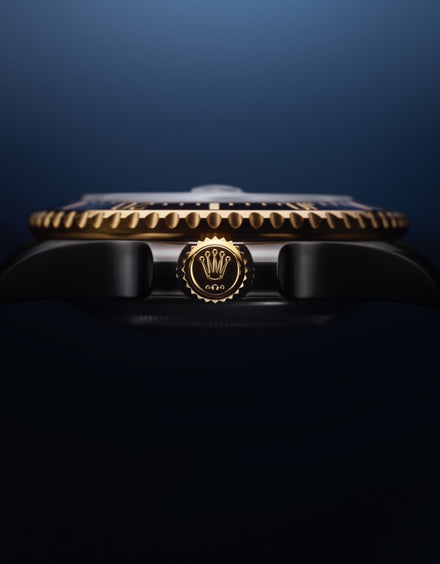 Side view of a luxury watch crown with a gold Rolex logo and a gold-edged bezel against a dark background.