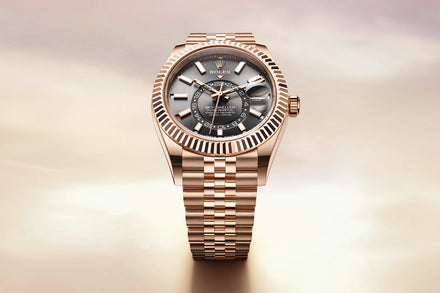 A gold Rolex watch with a black dial and metal bracelet displayed against a soft, blurred background.