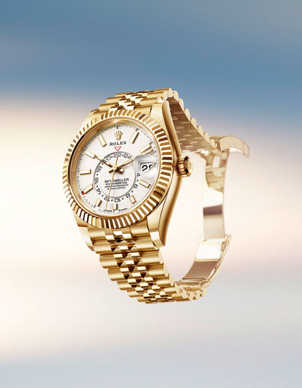 A gold Rolex watch with a white dial and date display, shown against a soft, blurred sky background.