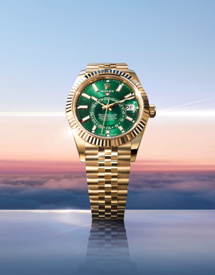 A gold Rolex watch with a green face is displayed against a sky at sunrise above the clouds.