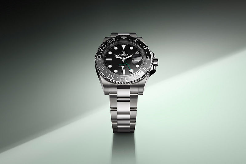 A stainless steel Rolex watch with a black dial and bezel on a gradient green background.
