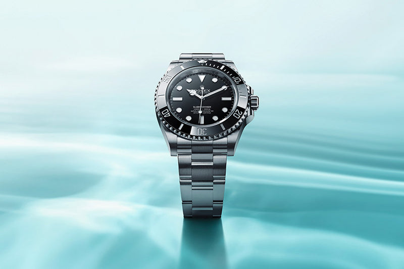 A silver luxury wristwatch with a black dial is displayed upright on a smooth, aqua-blue background.