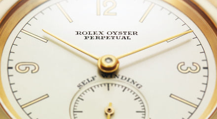 Close-up of a Rolex Oyster Perpetual watch face with gold hands and hour markers.