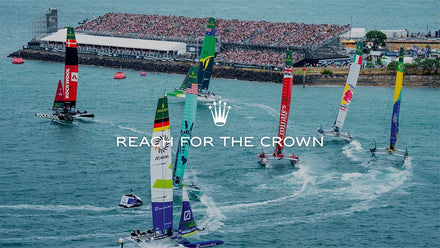Sailboats racing in a body of water with a large crowd in the background, featuring the Rolex logo.