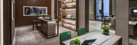 Modern, elegant watch boutique interior with display cases, wooden shelves, and green-accented furniture.