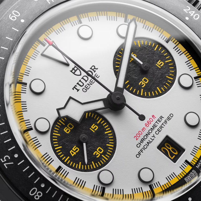 Chronograph watch face with white dial, black subdials with yellow markers, and yellow-accented bezel.