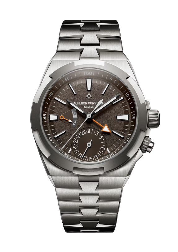 Stainless steel watch with dark brown dial, dual time zone subdial, orange triangle indicator, and metal bracelet.