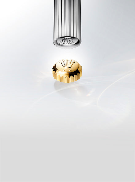 A gold Rolex crown winding crown below a silver mechanical tool against a light, minimalist background.