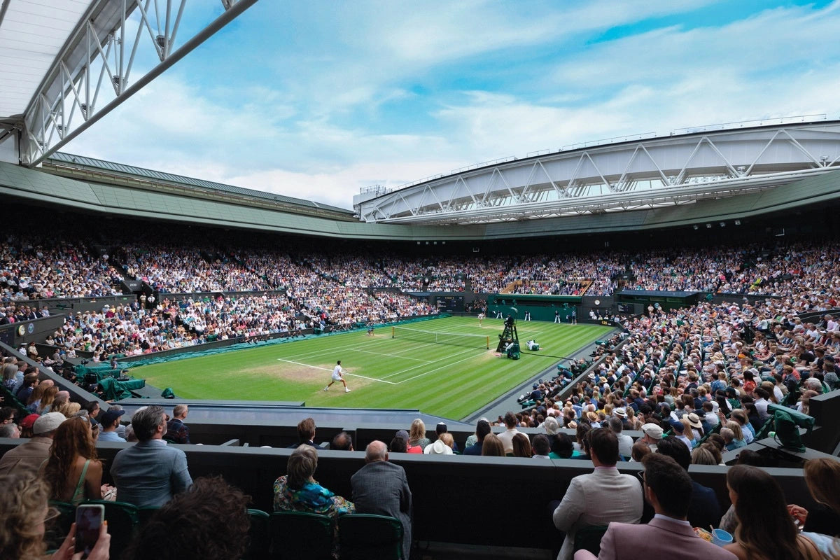 Wide view of a crowded tennis stadium during a match with players on the court under a partly open roof.