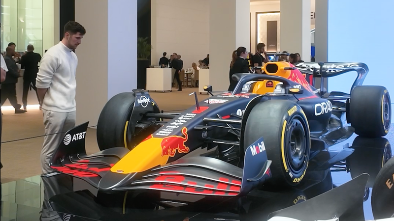 A man stands next to a Red Bull Racing Formula 1 car displayed indoors at an event.